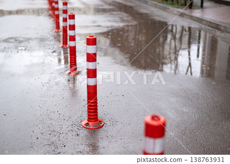 Red and white reflective traffic bollards on a wet asphalt road with puddles after rain 138763931