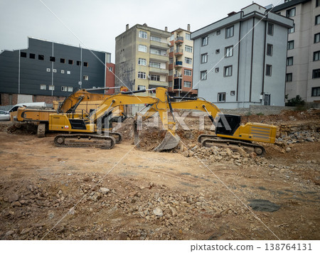 Two yellow excavators working at a city construction site 138764131