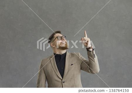 Elegant man with a happy expression looking up raises his index finger on a gray background. 138764150