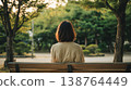 一位女士坐在公園長椅上，背對著鏡頭，凝視著綠樹。 138764449
