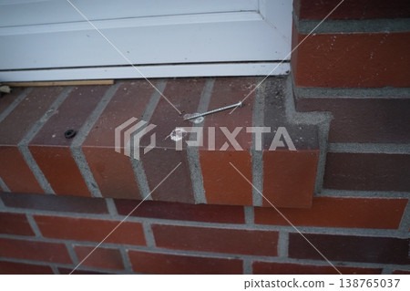 Metal tool lying on a brick ledge below a white frame, with dust and small debris on the surface. A close-up of a tool on a masonry step. Metal tool lying on a brick ledge below a white frame, with dust and small debris on the surface. A close-up of a tool on a masonry step. 138765037