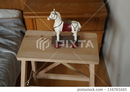 Wooden toy horse with red saddle on a small table beside a bed and dresser. Simple indoor still life scene. Wooden toy horse with red saddle on a small table beside a bed and dresser. Simple indoor still life scene. 138765085
