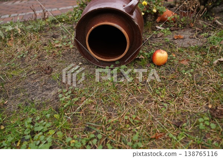 Large clay jar lying on grass in a garden bed, with apples scattered nearby and a brick path in the background Large clay jar lying on grass in a garden bed, with apples scattered nearby and a brick path in the background 138765116
