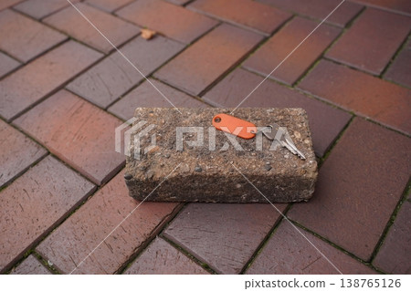 Key on orange keychain resting on a concrete brick on a paved sidewalk Key on orange keychain resting on a concrete brick on a paved sidewalk 138765126