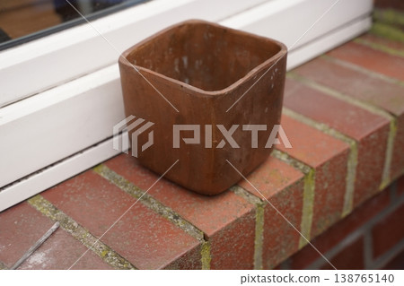 Brown square planter on a brick ledge beside a white frame Brown square planter on a brick ledge beside a white frame 138765140