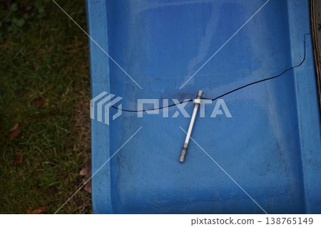 Cracked blue plastic panel with a small metal pin or bolt lying across the fracture line on an outdoor surface 138765149