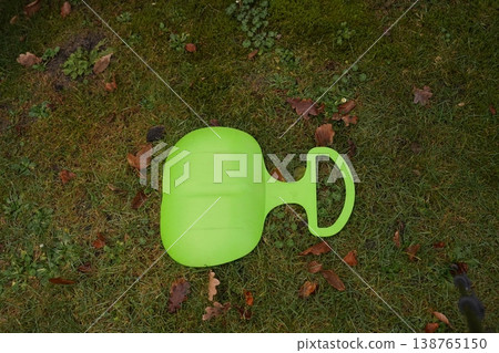 Green plastic garden sled on grass with fallen leaves 138765150