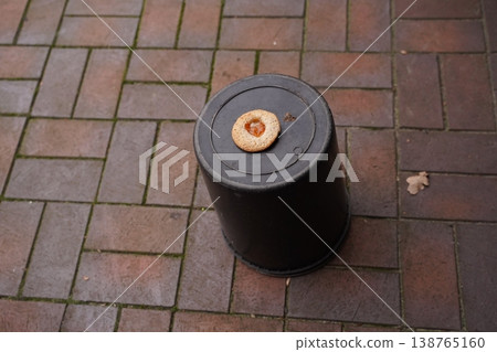 Bagel on upside-down black plastic bucket on brick pavement outdoors 138765160
