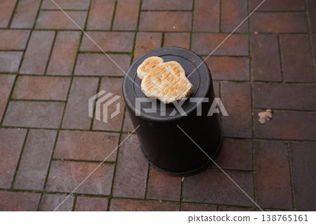 Heart-shaped pastry on a black plastic bucket lid on brick pavement 138765161