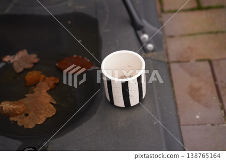Paper cup with striped pattern on a bin lid near fallen autumn leaf on pavement Paper cup with striped pattern on a bin lid near fallen autumn leaf on pavement 138765164