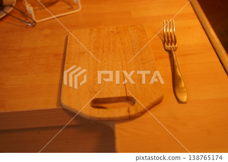 Wooden cutting board on a table beside a fork, with eyeglasses in the corner Wooden cutting board on a table beside a fork, with eyeglasses in the corner 138765174