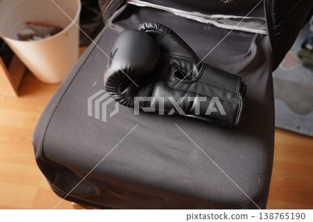 Black boxing glove resting on a padded bench in a gym corner, with a bucket in the background Black boxing glove resting on a padded bench in a gym corner, with a bucket in the background 138765190