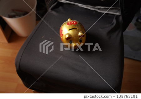 Small golden piggy bank with red decorations on a black fabric seat near a bucket on a wooden floor Small golden piggy bank with red decorations on a black fabric seat near a bucket on a wooden floor 138765191
