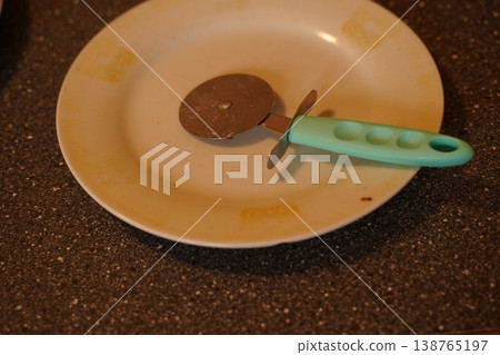 Round metal cutter with blue handle on an empty ceramic plate on a speckled countertop Round metal cutter with blue handle on an empty ceramic plate on a speckled countertop 138765197