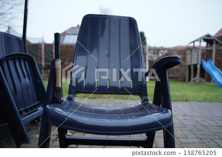 Dark plastic patio chair in close-up on a paved yard, with another chair beside it and a garden in the background. An outdoor seating scene. 138765205