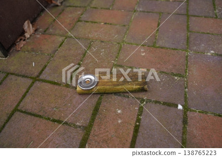 Wooden plank with a metal can lid on brick paving, outdoors near a wall 138765223