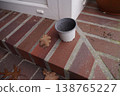 Empty plastic pot on brick step near a doorway, with fallen dry leaf on the ground 138765227