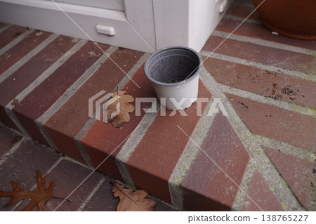 Empty plastic pot on brick step near a doorway, with fallen dry leaf on the ground 138765227