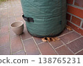 Green fabric container on tiled floor near brick wall, with beige cup and dry leaf beside it 138765231