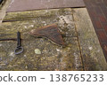Rusty metal shard and a key lying on a weathered wooden tabletop near brick paving 138765233