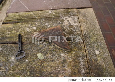 Rusty metal shard and a key lying on a weathered wooden tabletop near brick paving 138765233