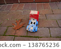 Dirty red and blue toy truck on brick pavement with a fallen brown leaf nearby 138765236