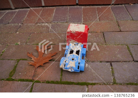 Dirty red and blue toy truck on brick pavement with a fallen brown leaf nearby 138765236