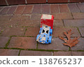 Small toy vehicle on brick pavement beside a dry leaf; red and blue plastic, worn and dirty, outdoors 138765237