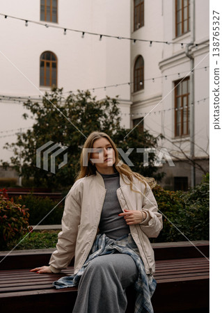 Woman sitting on a bench in a courtyard during the afternoon near a historic building Woman sitting on a bench in a courtyard during the afternoon near a historic building 138765327