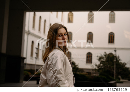 Young woman standing outdoors in a courtyard with buildings in the background during daytime Young woman standing outdoors in a courtyard with buildings in the background during daytime 138765329