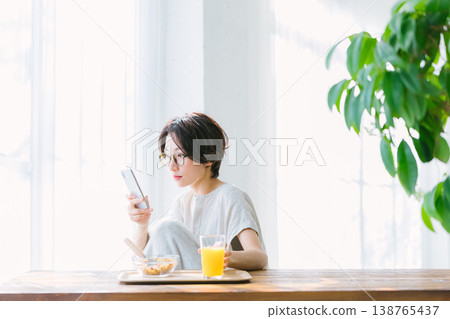 Woman eating breakfast while looking at smartphone Woman eating breakfast while looking at smartphone 138765437