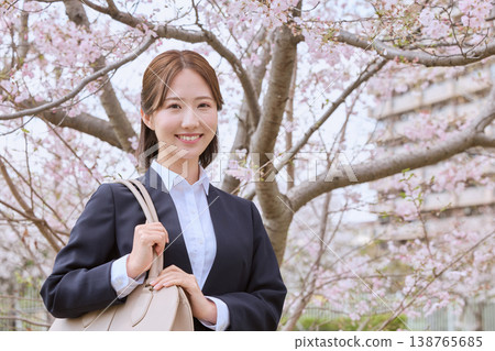 一位身著職業套裝的年輕女子在櫻花樹下微笑——這是一幅春季求職的畫面。 138765685