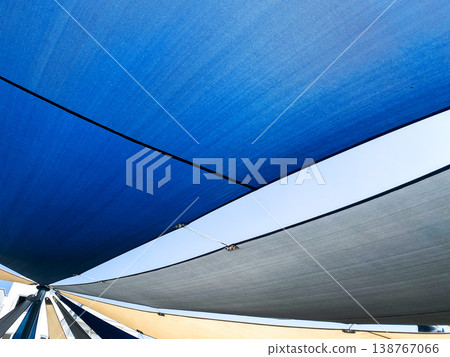Colorful shade sails in outdoor location to provide from sun, closeup. Multiple sails in different shades of blue and gray, comfortable spot. Bright sunlight shining through gaps between sails 138767066