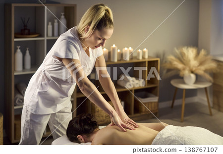 Professional masseuse giving relaxing back massage in spa with candles and decor Professional masseuse giving relaxing back massage in spa with candles and decor 138767107