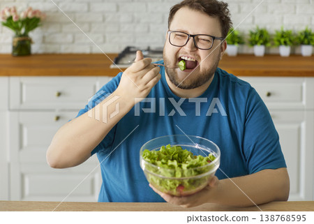 Plus-size man enjoying fresh green salad at home kitchen, healthy diet concept 138768595