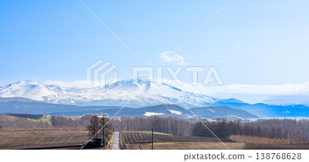 A magnificent view of the Daisetsuzan mountain range, including Mt. Asahidake and a road, as seen from the area around Biei Town, Hokkaido in spring. A magnificent view of the Daisetsuzan mountain range, including Mt. Asahidake and a road, as seen from the area around Biei Town, Hokkaido in spring. 138768628