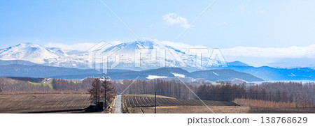 A magnificent view of the Daisetsuzan mountain range, including Mt. Asahidake and a road, as seen from the area around Biei Town, Hokkaido in spring. A magnificent view of the Daisetsuzan mountain range, including Mt. Asahidake and a road, as seen from the area around Biei Town, Hokkaido in spring. 138768629