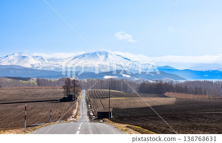 A magnificent view of the Daisetsuzan mountain range, including Mt. Asahidake and a road, as seen from the area around Biei Town, Hokkaido in spring. A magnificent view of the Daisetsuzan mountain range, including Mt. Asahidake and a road, as seen from the area around Biei Town, Hokkaido in spring. 138768631
