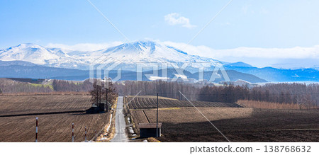 A magnificent view of the Daisetsuzan mountain range, including Mt. Asahidake and a road, as seen from the area around Biei Town, Hokkaido in spring. A magnificent view of the Daisetsuzan mountain range, including Mt. Asahidake and a road, as seen from the area around Biei Town, Hokkaido in spring. 138768632