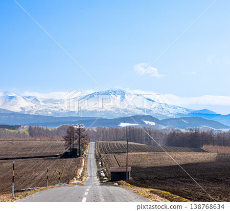 A magnificent view of the Daisetsuzan mountain range, including Mt. Asahidake and a road, as seen from the area around Biei Town, Hokkaido in spring. A magnificent view of the Daisetsuzan mountain range, including Mt. Asahidake and a road, as seen from the area around Biei Town, Hokkaido in spring. 138768634