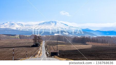 A magnificent view of the Daisetsuzan mountain range, including Mt. Asahidake and a road, as seen from the area around Biei Town, Hokkaido in spring. A magnificent view of the Daisetsuzan mountain range, including Mt. Asahidake and a road, as seen from the area around Biei Town, Hokkaido in spring. 138768636