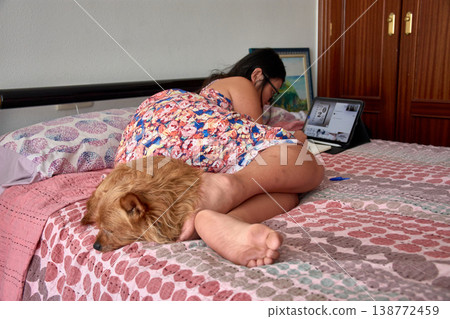 Young woman lying in bed looking at her tablet next to her sleeping dog during a relaxing afternoon at home 138772459