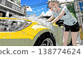 A young woman washing her car on a sunny day | A refreshing lifestyle scene with blue skies and splashing water. 138774624