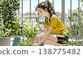 A young woman watering flowers in a planter | A refreshing scene of balcony gardening and enjoying nature. 138775482