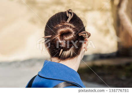Woman with a neat bun secured by decorative wooden hair sticks wearing a blue coat outdoors Woman with a neat bun secured by decorative wooden hair sticks wearing a blue coat outdoors 138776781