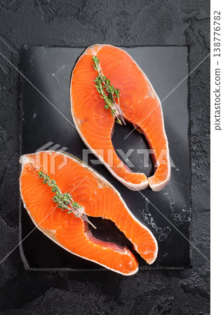 Fresh uncooked salmon steaks red fish types on black slate, herbs and dark textured background for cooking Fresh uncooked salmon steaks red fish types on black slate, herbs and dark textured background for cooking 138776782