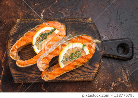 Closeup grilled salmon steaks chum with juicy texture and char marks, thyme and lemon on dark background Closeup grilled salmon steaks chum with juicy texture and char marks, thyme and lemon on dark background 138776793