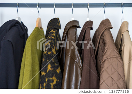 A row of autumn, winter and spring coats in earthy tones hanging on a sleek clothing rack. A row of autumn, winter and spring coats in earthy tones hanging on a sleek clothing rack. 138777316