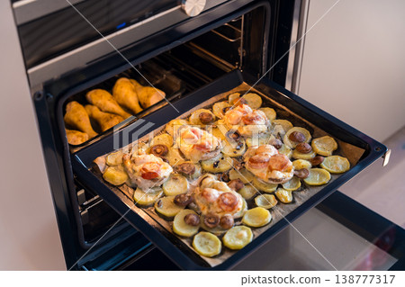 A baking tray with French-style pork, potatoes, mushrooms, and cheese, alongside baked chicken A baking tray with French-style pork, potatoes, mushrooms, and cheese, alongside baked chicken 138777317
