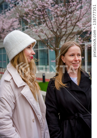 Two caucasian women dressed in stylish coats are smiling and walking outdoors in an urban area Two caucasian women dressed in stylish coats are smiling and walking outdoors in an urban area 138777351